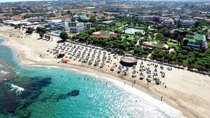 Una località balneare con una spiaggia sabbiosa ampia, acque cristalline color turchese e numerosi ombrelloni e lettini.