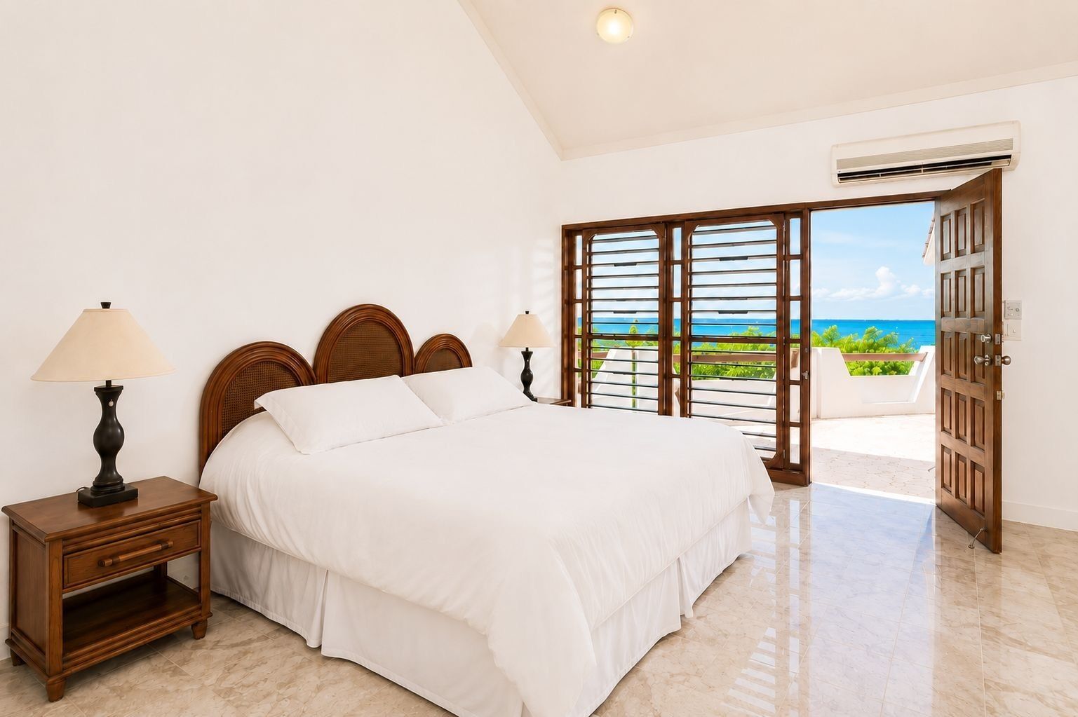A bedroom with a bed, nightstand, lamp, and a view of the ocean through a door.