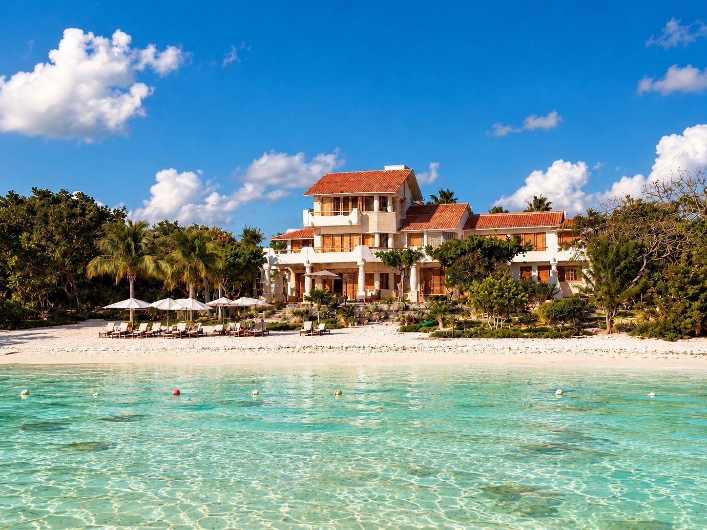 A beachfront property with a large building, clear turquoise water, and lush greenery.