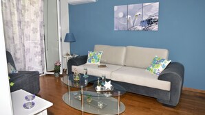 A modern living room with a glass coffee table, a sofa with patterned cushions, a side table with a lamp, and a wall-mounted air conditioner. - The ideal house at the foot of Acropolis. (Athina)