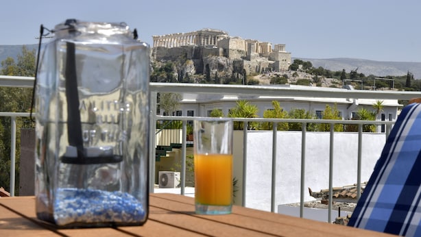 A clear view of the Parthenon on a sunny day from a balcony with a table featuring a glass jar and a glass of orange juice. - The ideal house at the foot of Acropolis. (Athina)