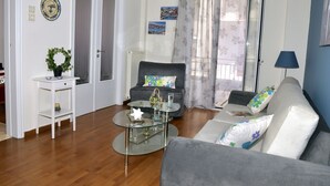 A living room with a grey sofa, a glass coffee table, a white armchair, and a small white side table. - The ideal house at the foot of Acropolis. (Athina)