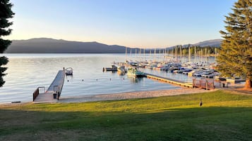 A marina with boats docked, a grassy area in the foreground, and mountains in the background.