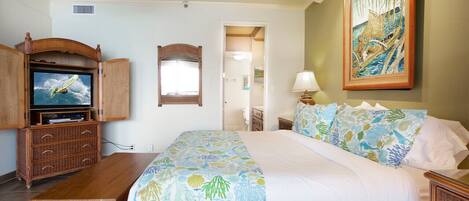 A bedroom with a bed, a television, a ceiling fan, a painting, and a door leading to another room.