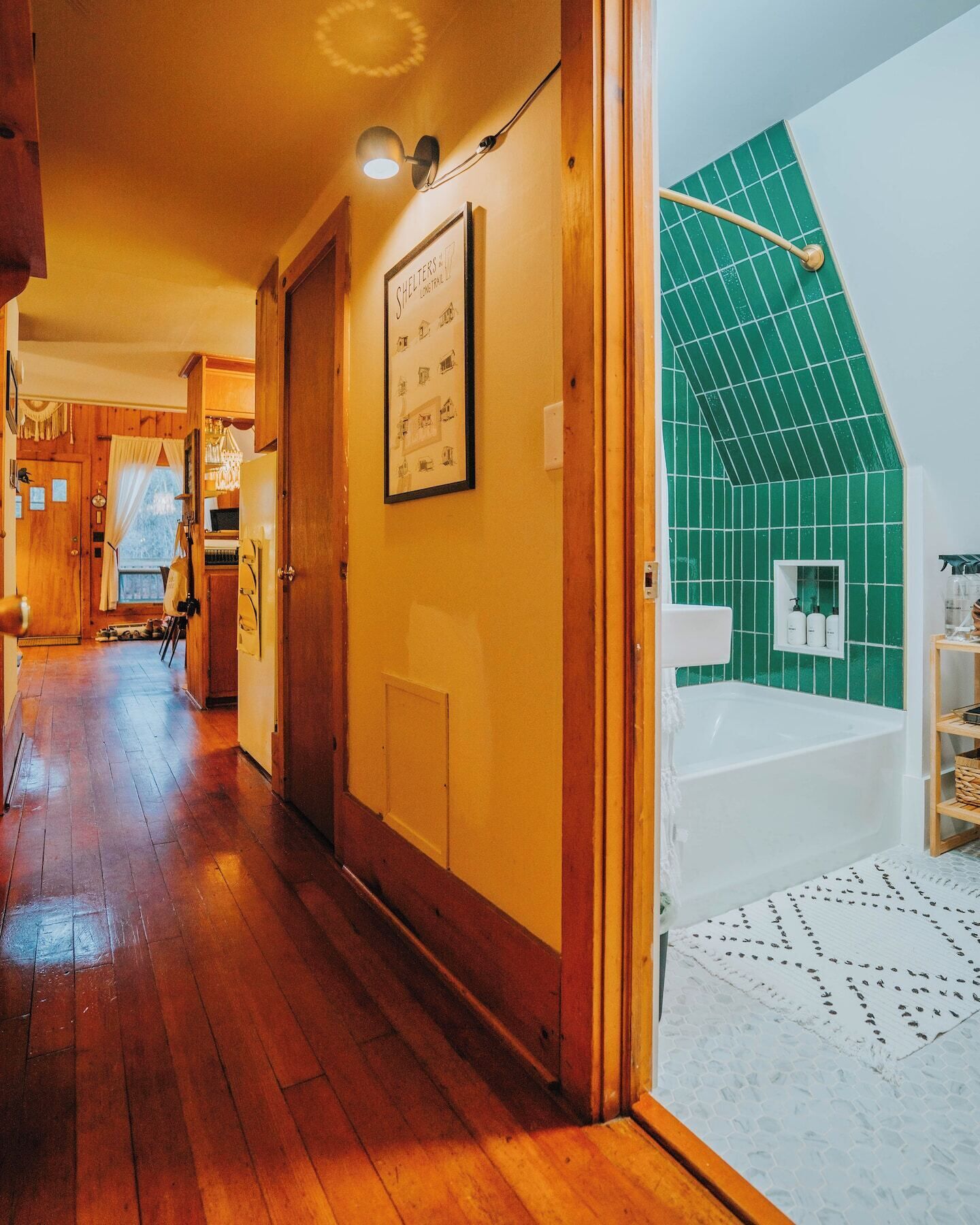 A hallway leading to a bathroom with a green-tiled shower area and a framed picture on the wall.