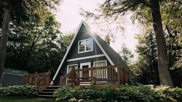 A cabin with a triangular roof, a wooden deck, and a front porch.