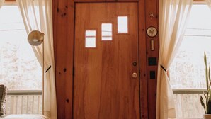 A wooden cabin with a large front door, two windows, and a hanging macrame decoration.