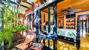 A room with a bed, a chair, a table, and a window overlooking greenery. -  Villa Oasis: A luxury villa just steps to beach with private pool, WIFI & A/C  (Tamarindo)