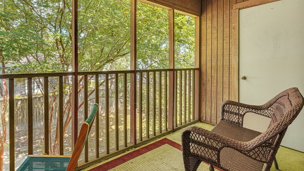 Une véranda avec un fauteuil en osier, une balustrade en bois et une vue sur les arbres à travers de grandes fenêtres.