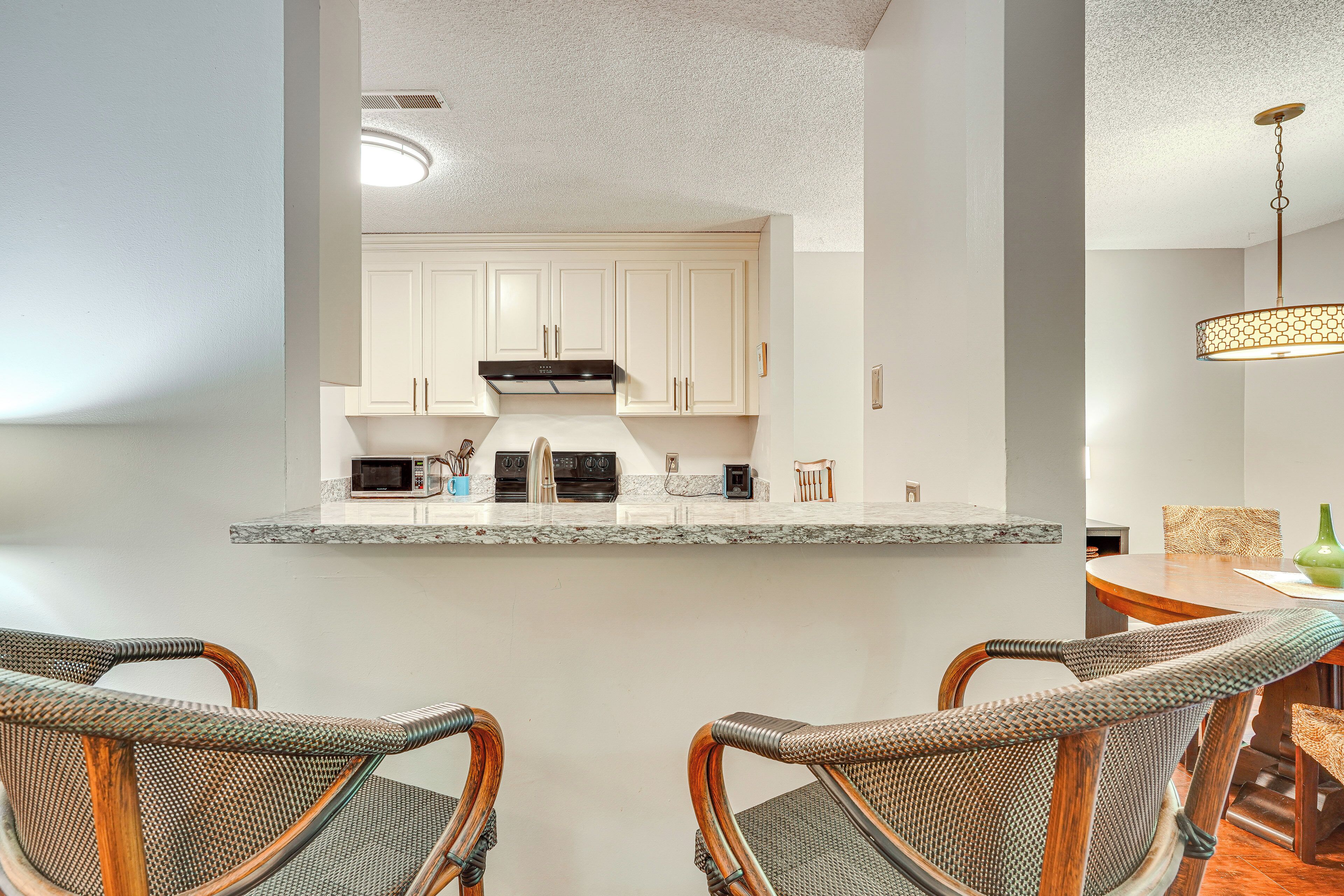 A kitchen with white cabinets, a microwave, and a stove. There are wicker chairs and a dining table with a vase.