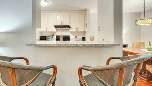 Une cuisine avec des meubles blancs, un four à micro-ondes et une cuisinière. On y trouve des chaises en osier et une table à manger agrémentée d’un vase.