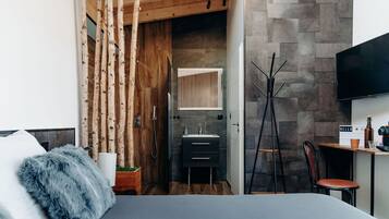 A modern bedroom with a bed, a wooden wardrobe, a bathroom with a sink and mirror, and a TV mounted on the wall.