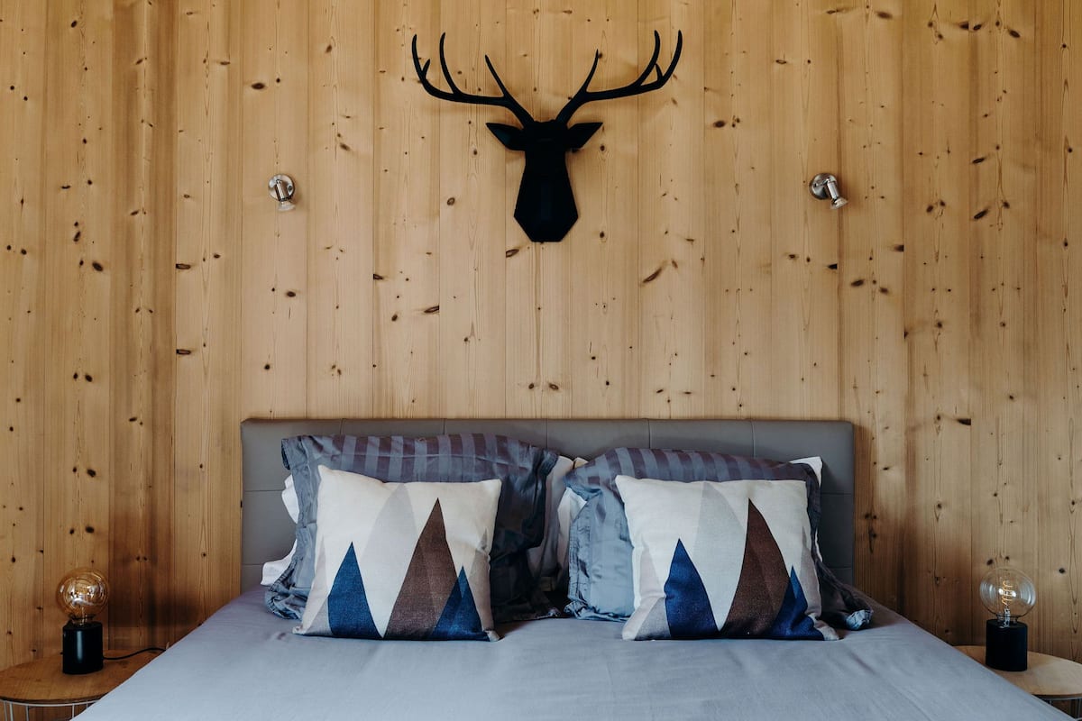 Une pièce aux murs lambrés, avec un lit, deux oreillers et une tête de cerf accrochée au mur.