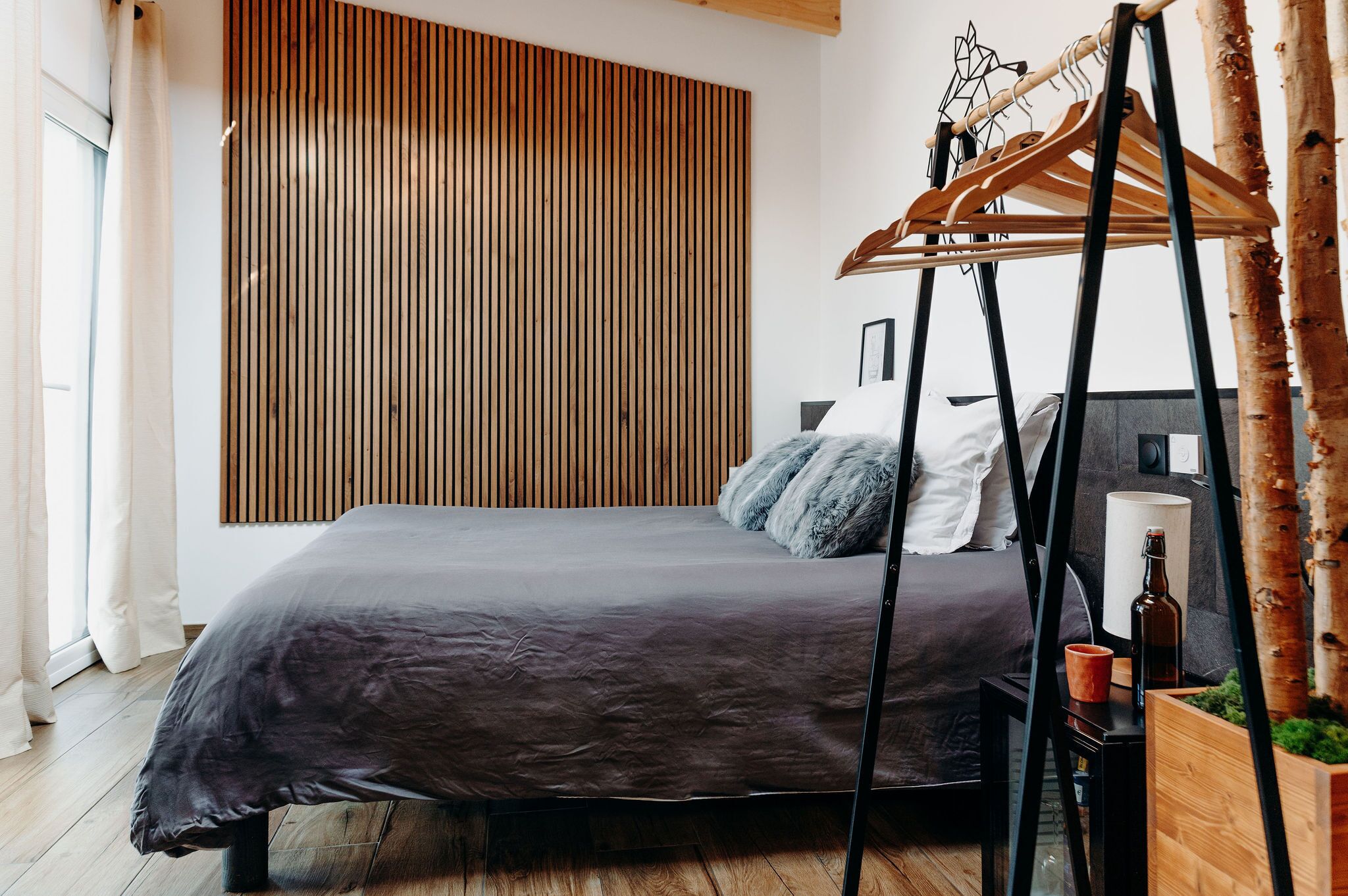 Une chambre moderne avec un lit, un mur recouvert de lambris en bois et un porte-manteau en bois.