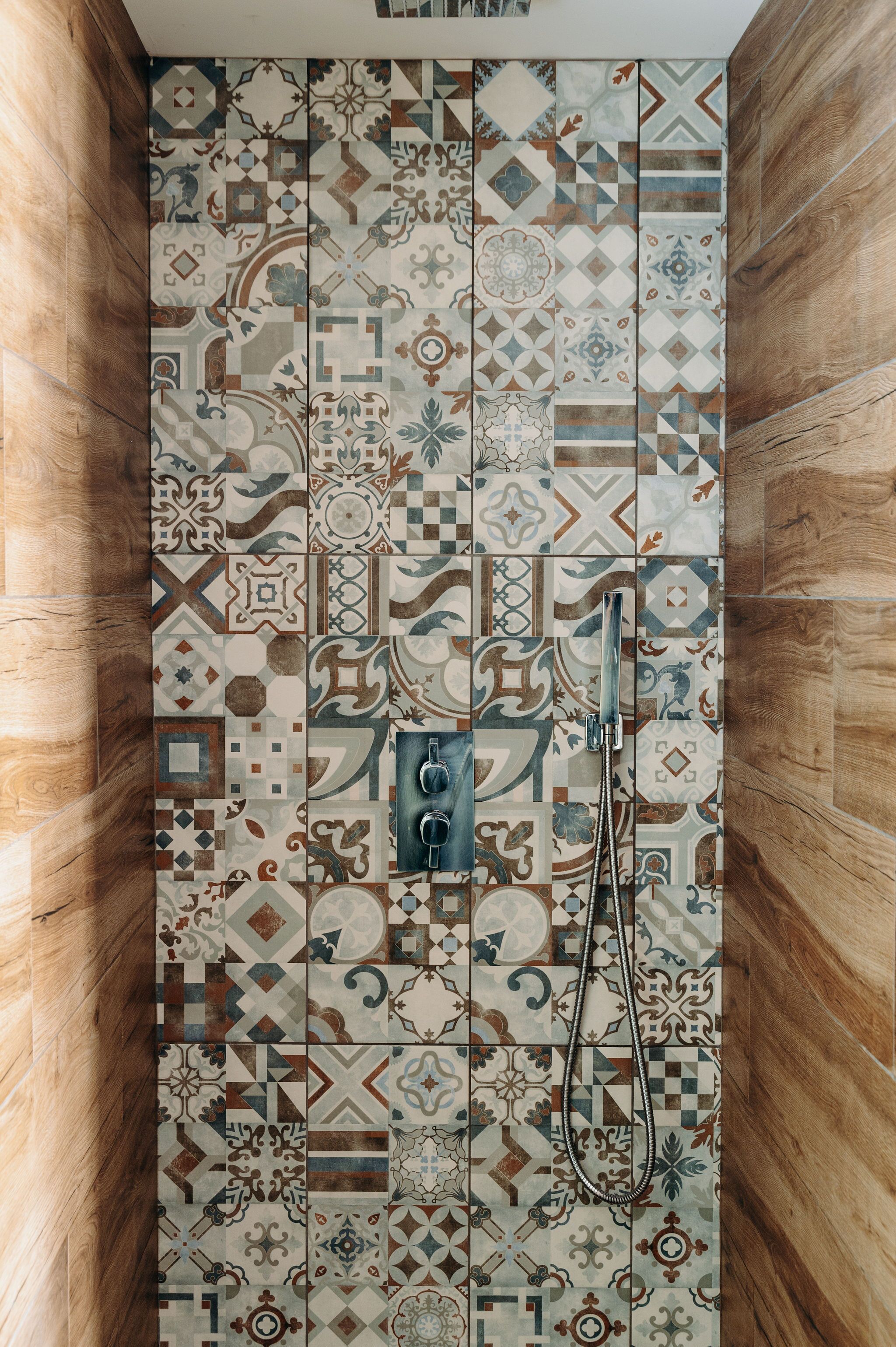 Une douche avec un mur recouvert de carreaux présentant une variété de motifs géométriques et floraux.