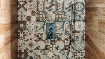 Une douche avec un mur recouvert de carreaux présentant une variété de motifs géométriques et floraux.