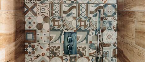 Ducha con pared de azulejos que presenta una variedad de diseños geométricos y florales.