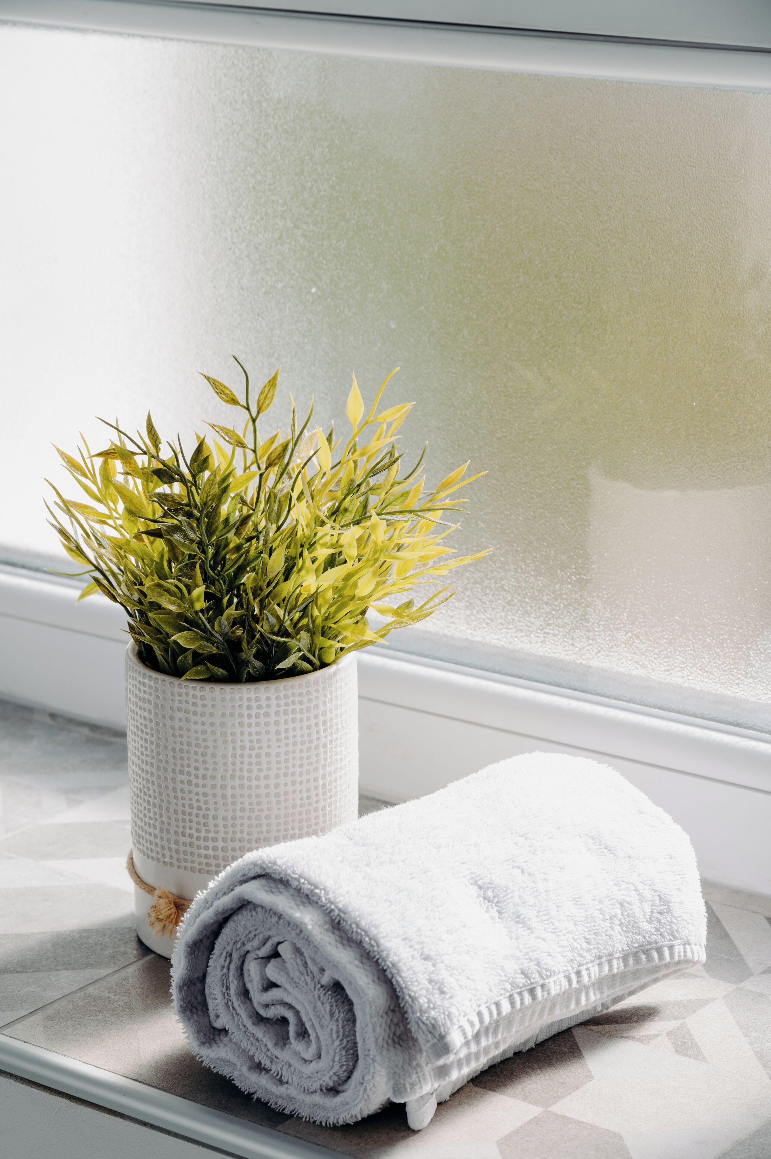 Ein Badezimmer mit einem weißen Handtuch, das aufgerollt ist, und einem Blumentopf auf der Fensterbank.