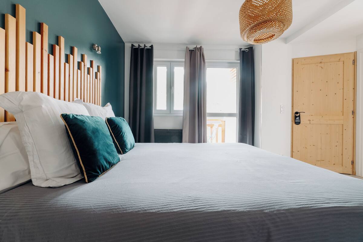 Une chambre à coucher avec un lit, une tête de lit en bois et une vue sur l’extérieur par une fenêtre.