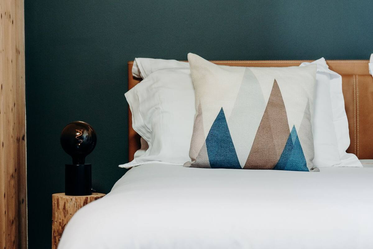 Un lit bien fait, avec une literie blanche, un coussin à motifs géométriques et une tête de lit en bois.