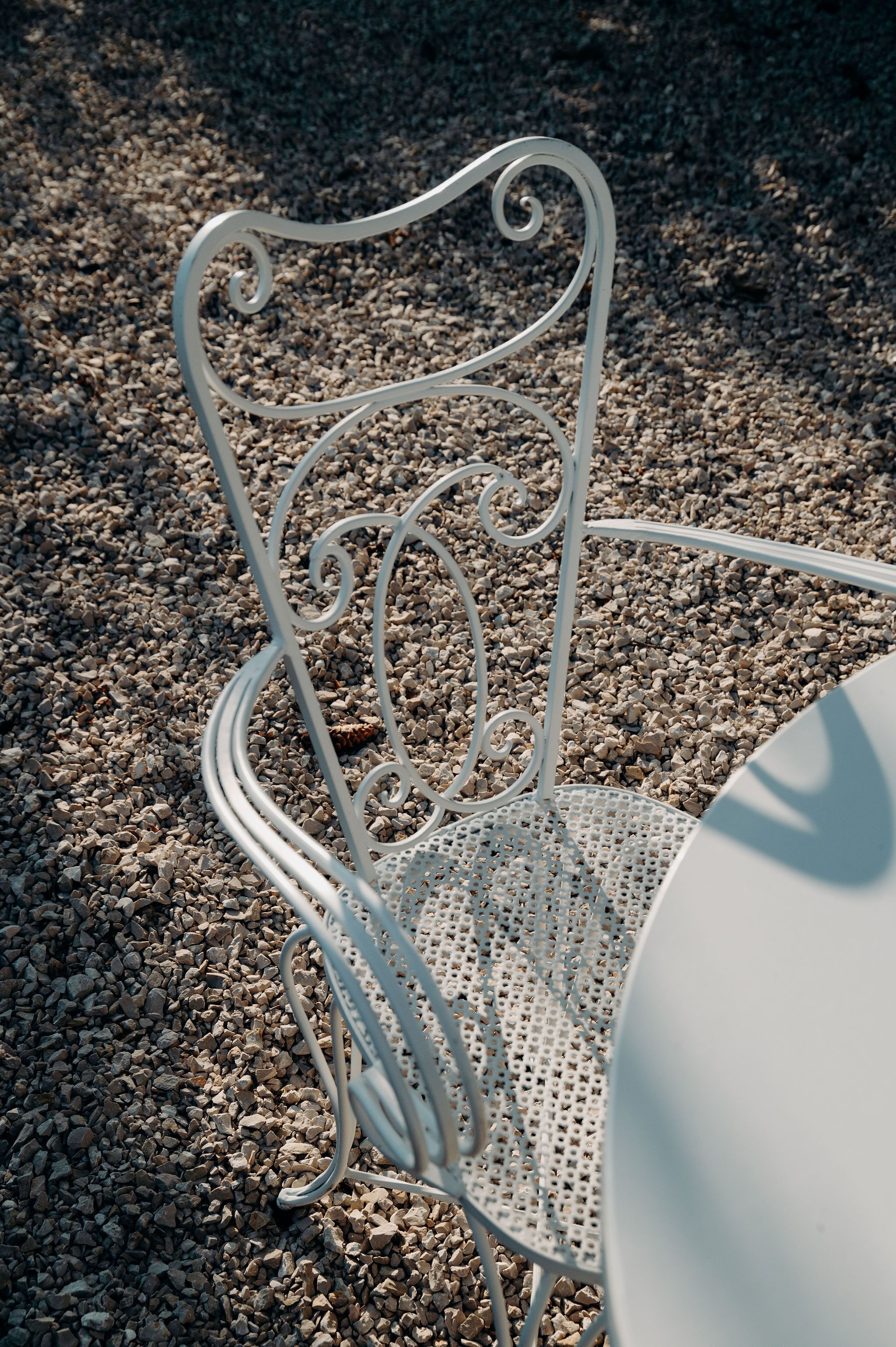 Una silla de metal con asiento y respaldo perforados, sobre una superficie de grava.