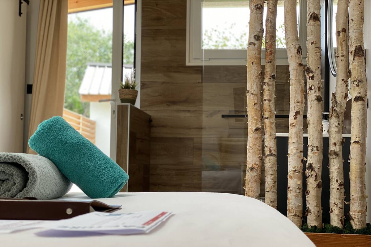 Un lit bien fait, avec des serviettes pliées, une tête de lit en bois et une fenêtre donnant sur un paysage verdoyant.