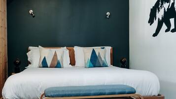 A bedroom with a wooden bed frame, a bench at the foot of the bed, and a wall with a black silhouette.