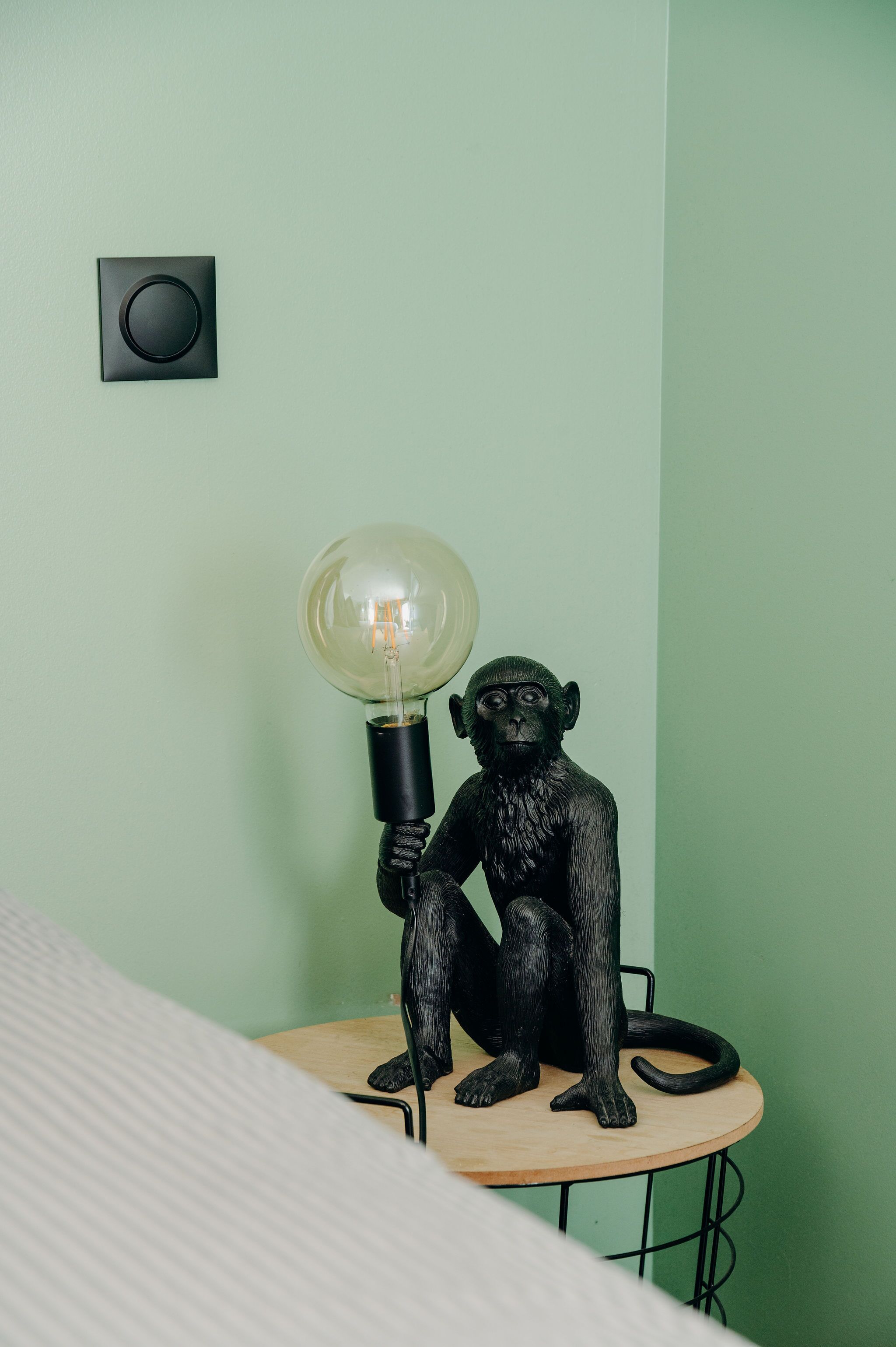 Una habitación con una pared verde, una pequeña mesa redonda y una estatua de mono negro sosteniendo una bombilla.