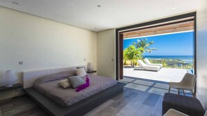 A bedroom with a bed, a nightstand, a chair, and a view of the ocean. - Luxury Villa Overlooking Orient Bay (SAINT MARTIN)