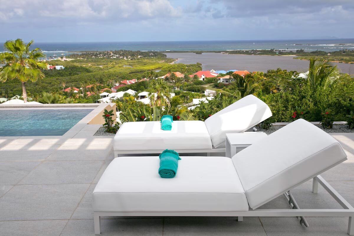 A poolside area with two white lounge chairs, one with a towel.