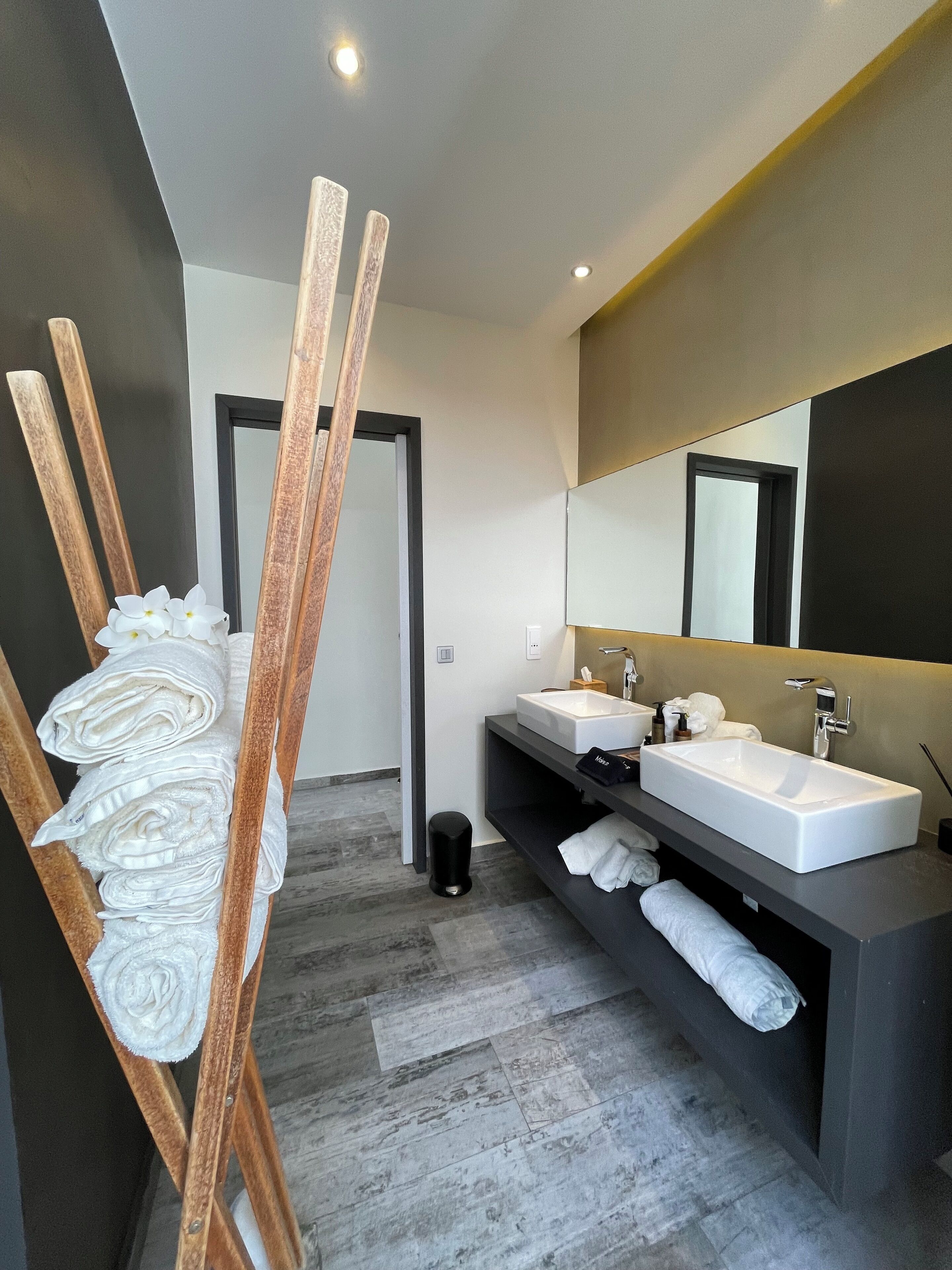 Un baño moderno con dos lavamanos, un espejo grande y un perchero de madera.