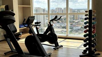 A gym with exercise equipment, a weight rack, and a large window with a city view.