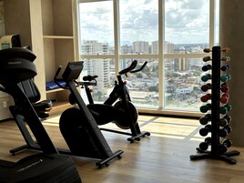 Uma academia com equipamentos de ginástica, suporte para pesos e uma ampla janela com vista para a cidade.