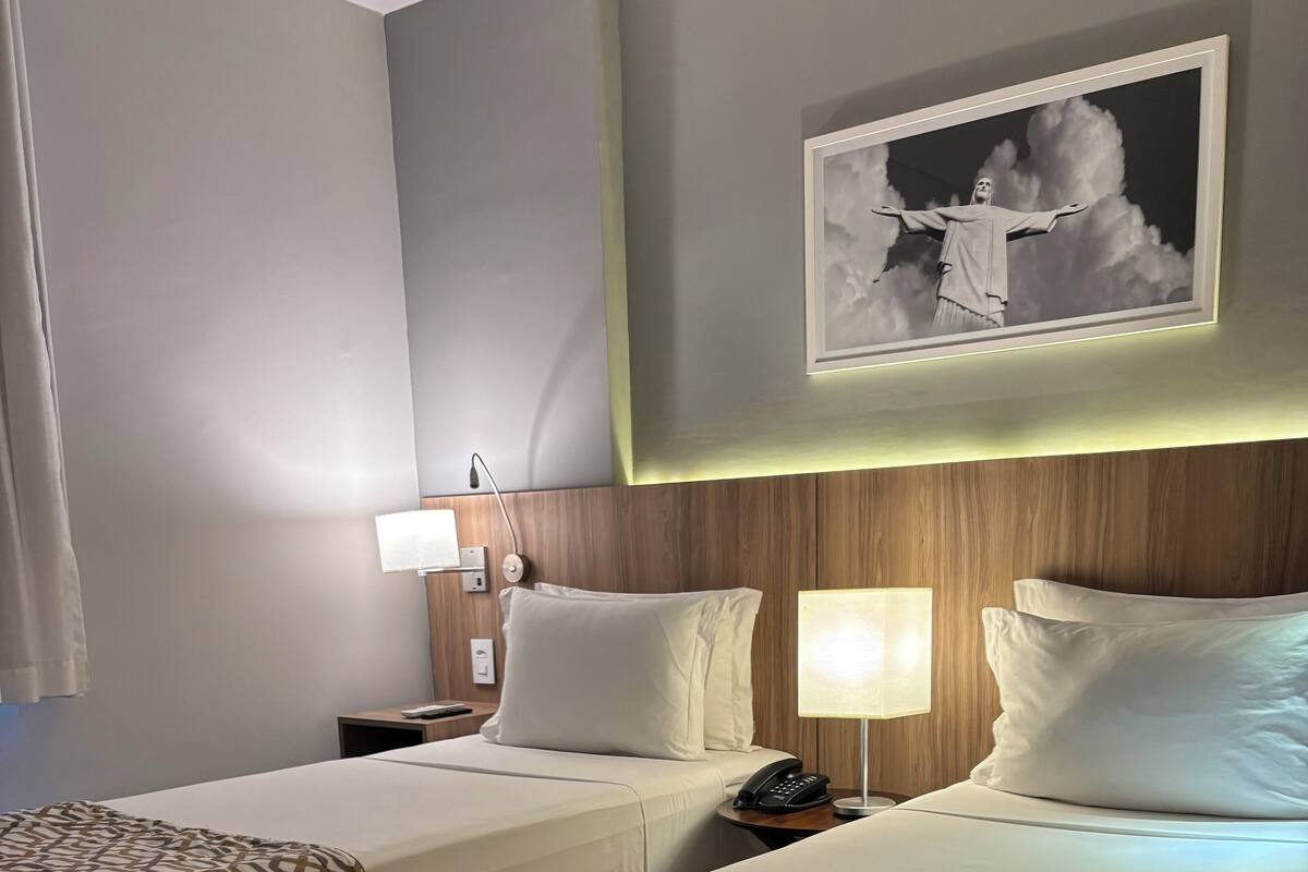 Een hotelkamer met twee bedden, een nachtkastje met een lamp, een telefoon en een lijst met een foto aan de muur.