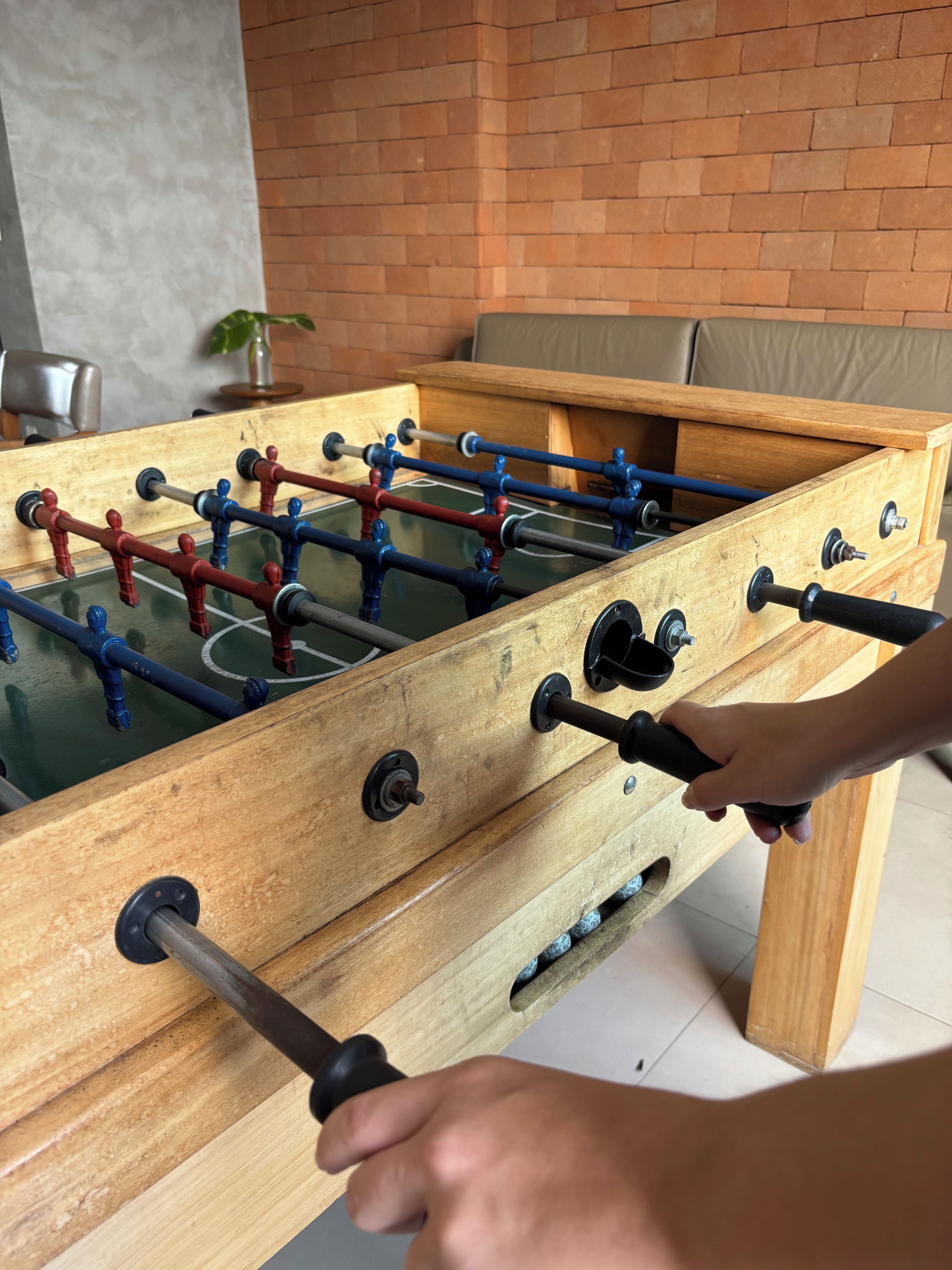 A wooden foosball table with metal rods and figures, set against a brick wall.