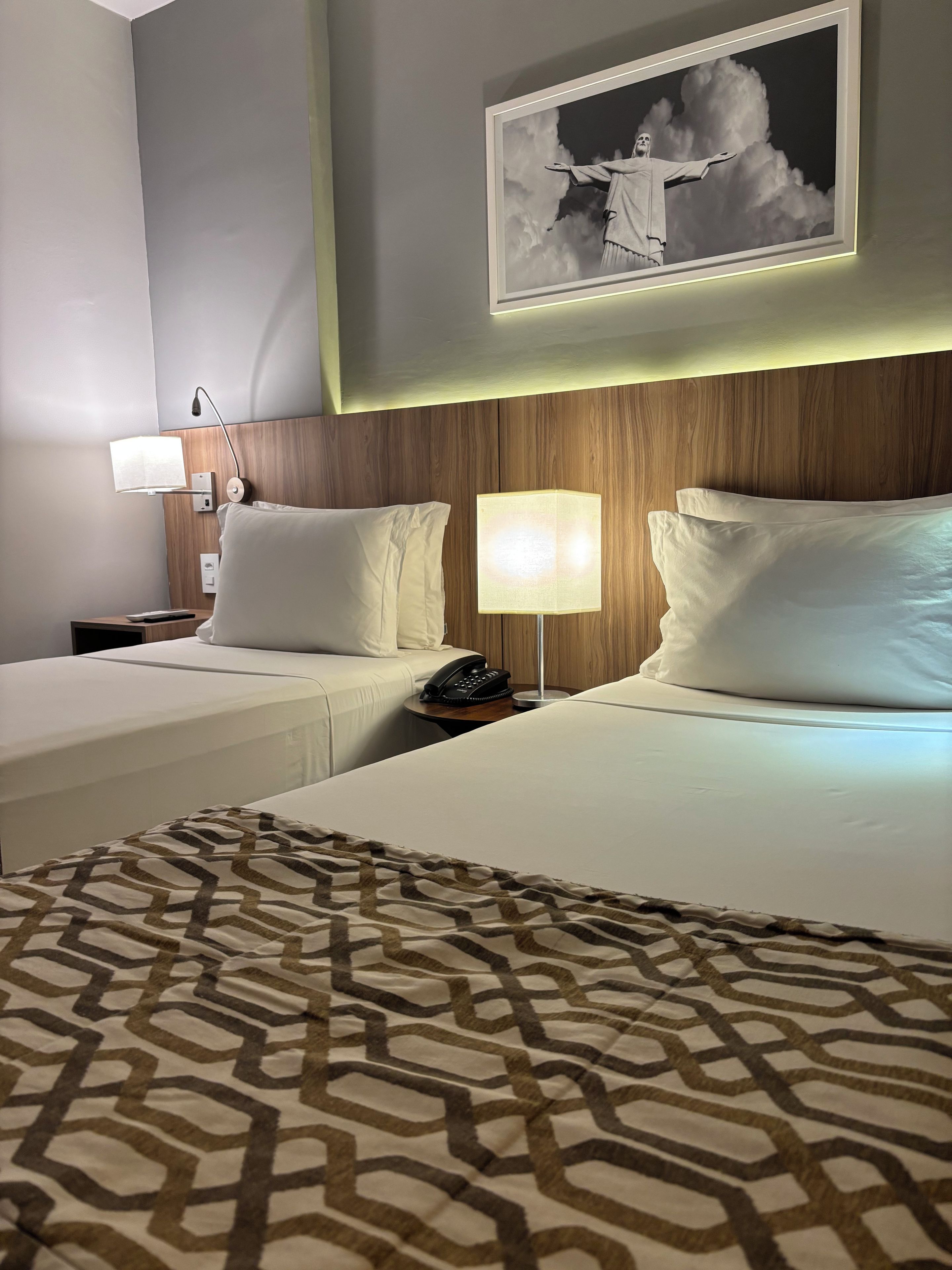 Habitación de hotel con dos camas, un plaid estampado, un cuadro enmarcado sobre las camas y una mesita de noche con una lámpara y teléfono.