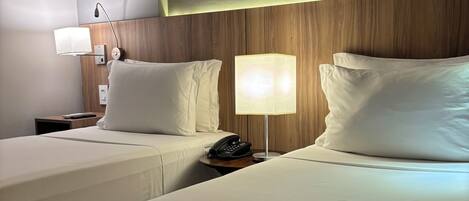 Habitación de hotel con dos camas, un plaid estampado, un cuadro enmarcado sobre las camas y una mesita de noche con una lámpara y teléfono.