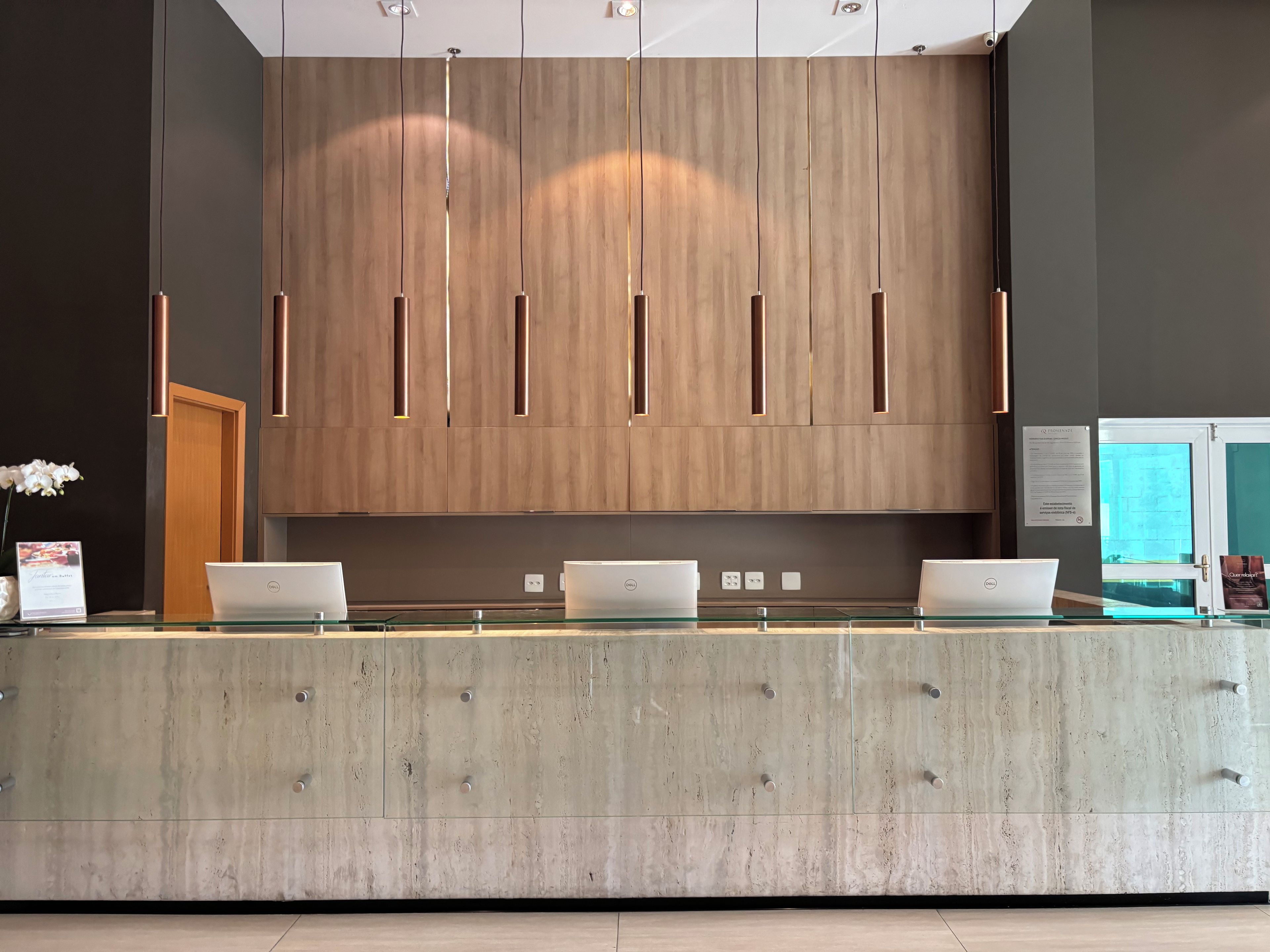 Una mesa de recepción con tres computadoras portátiles, paneles de madera y un mostrador de vidrio.