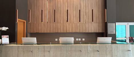 Una mesa de recepción con tres computadoras portátiles, paneles de madera y un mostrador de vidrio.