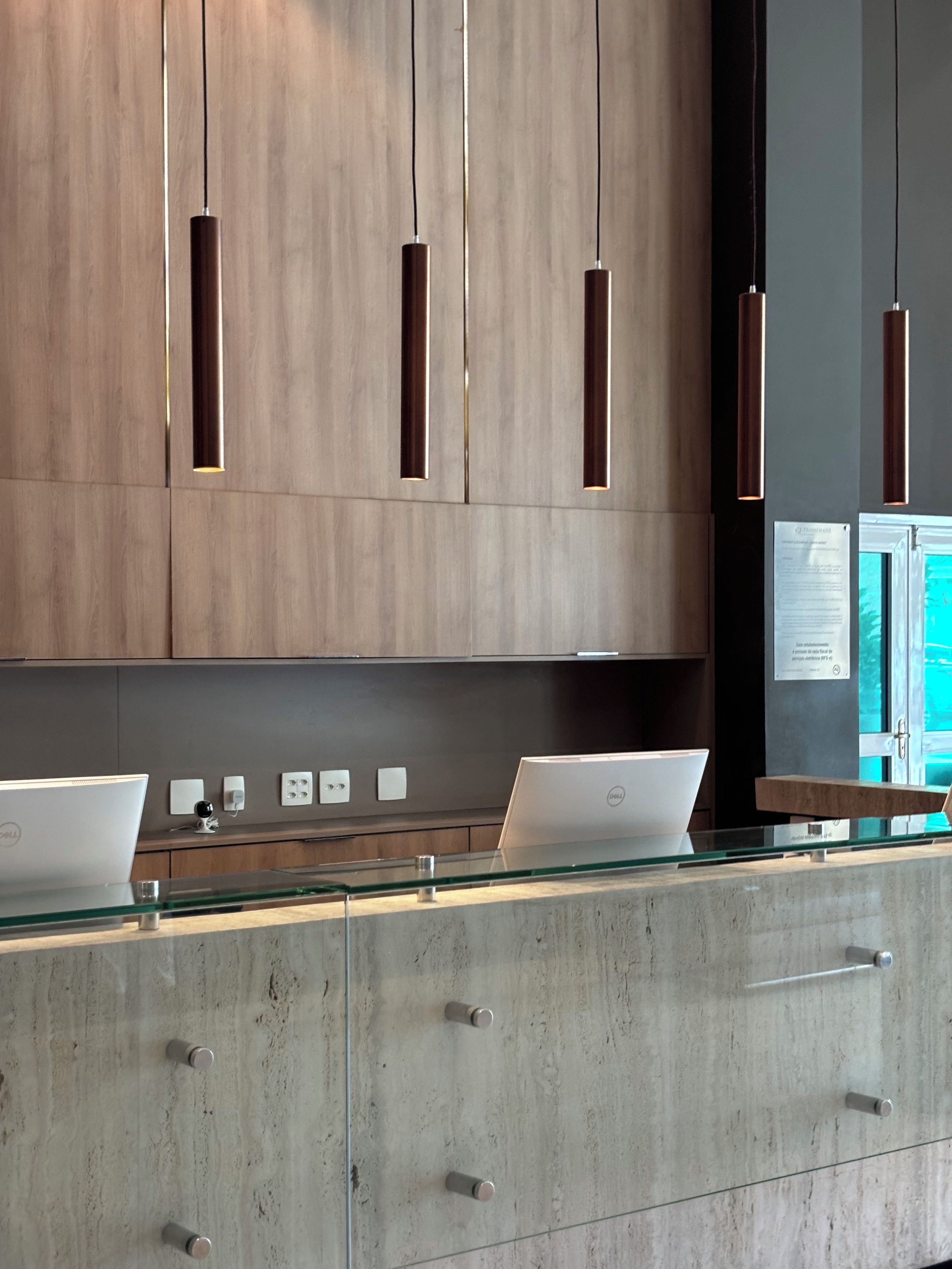 Una cucina moderna con mobili in legno, due laptop su un piano di vetro e lampade a sospensione.