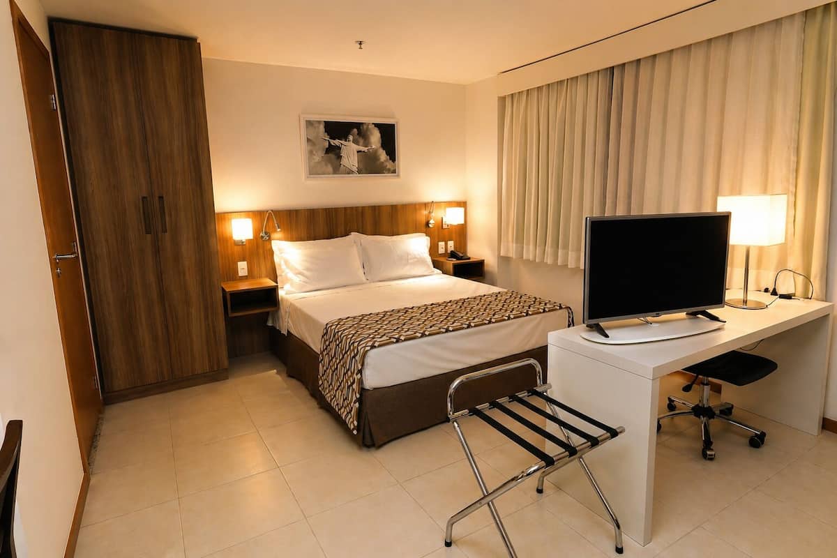 Een hotelkamer met een bed, bureau, stoel, televisie, nachtlampjes en een schilderij aan de muur.