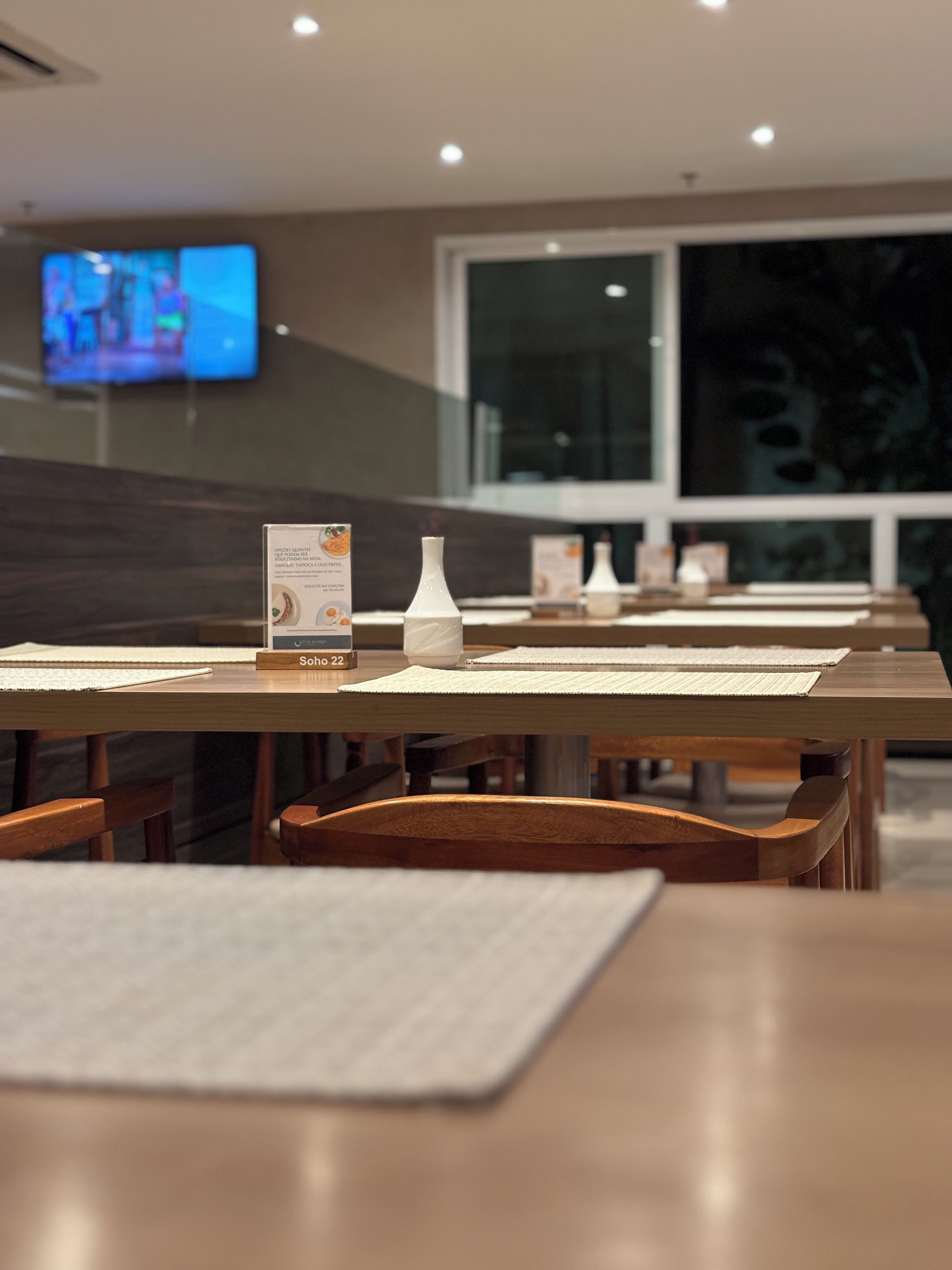 Un restaurant avec des tables dressées, un présentoir à menus et un écran de télévision en arrière-plan.
