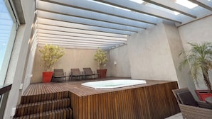 A modern outdoor terrace with a wooden reception desk, seating area, and potted plants. - Promenade Soho Campos dos Goytacazes (Campos)