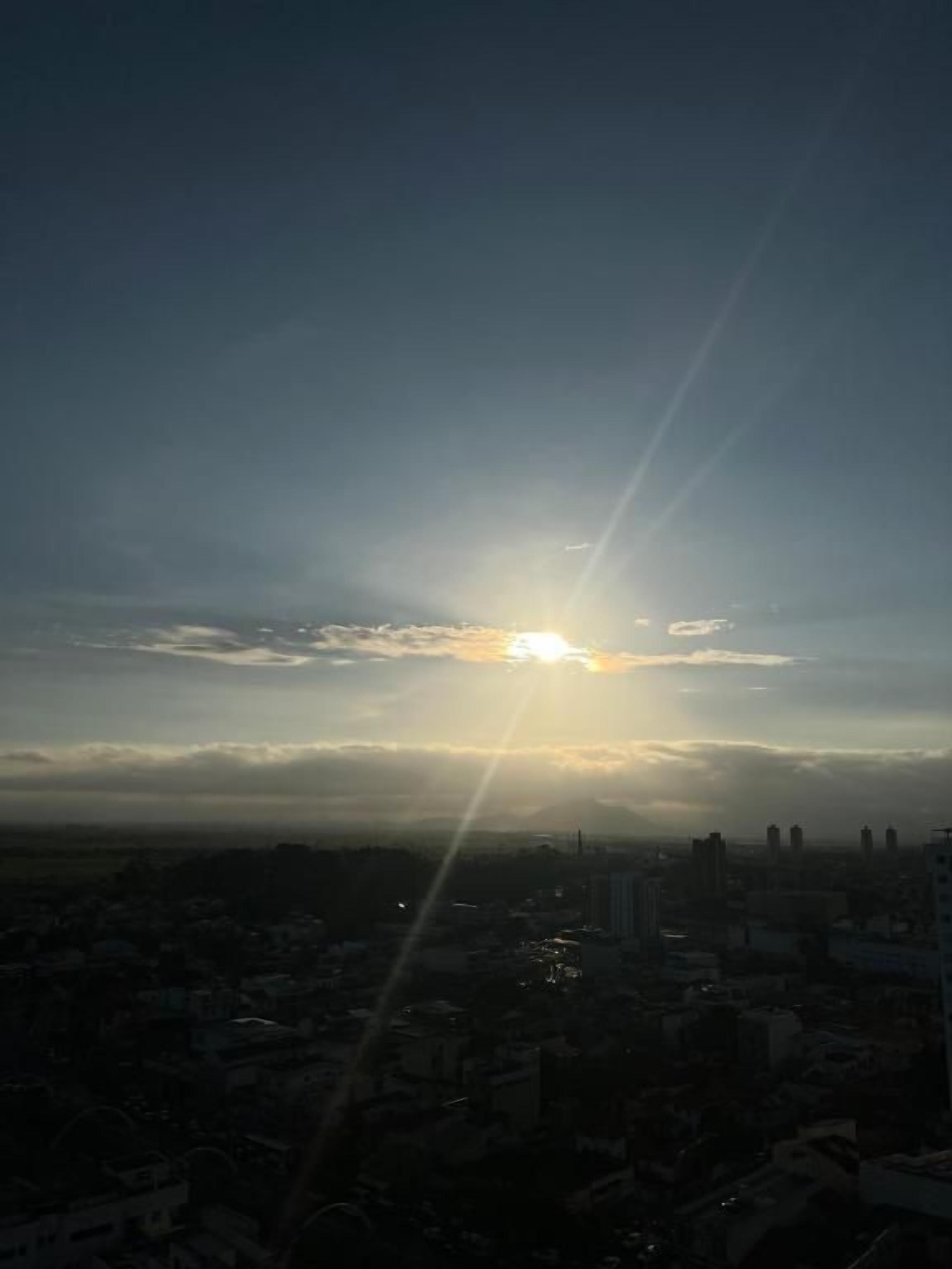 A cityscape with the sun setting behind clouds, casting rays of light.