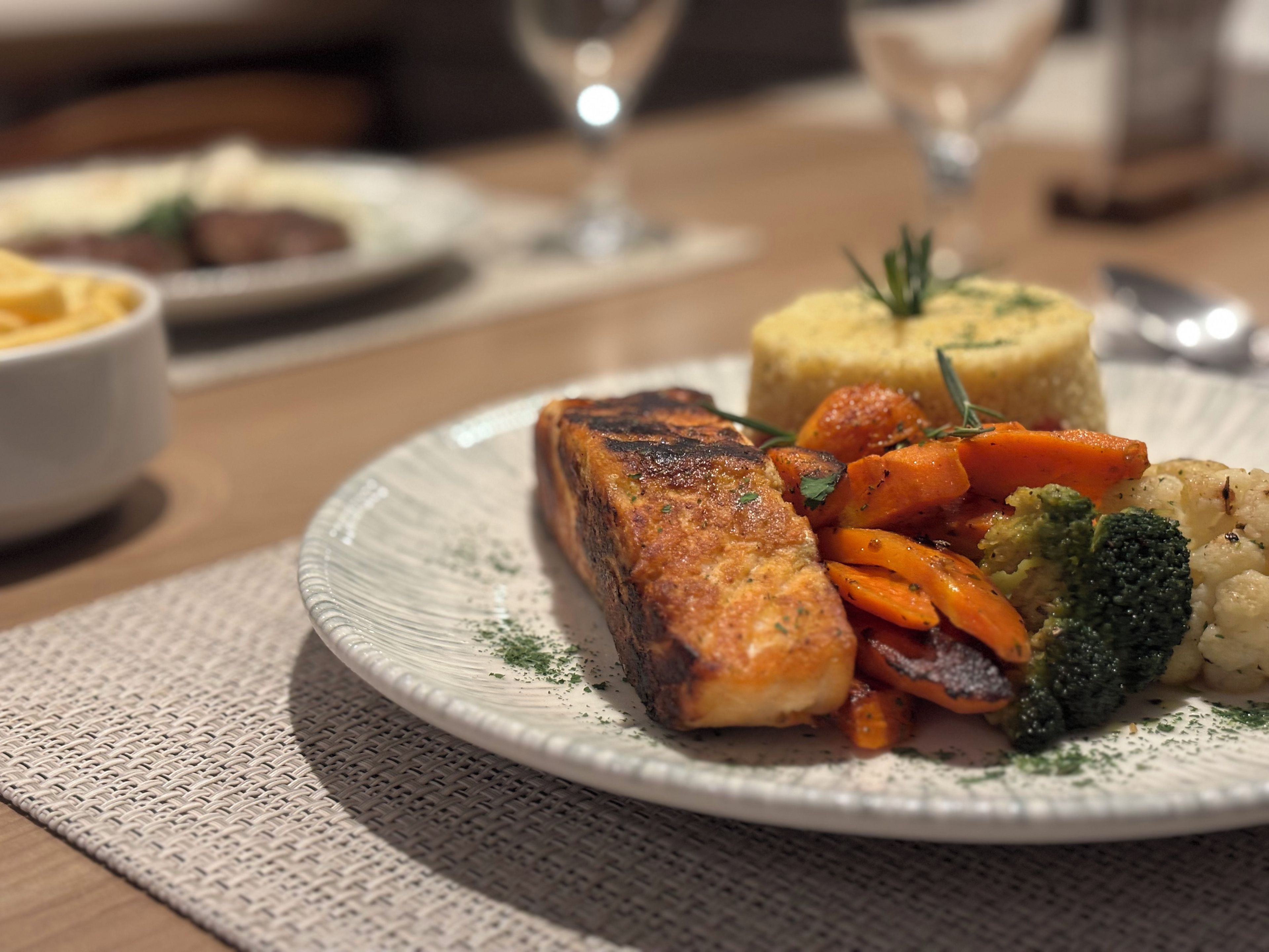 Une assiette de nourriture comprenant du saumon, des carottes, des brocolis et de la purée de pommes de terre.