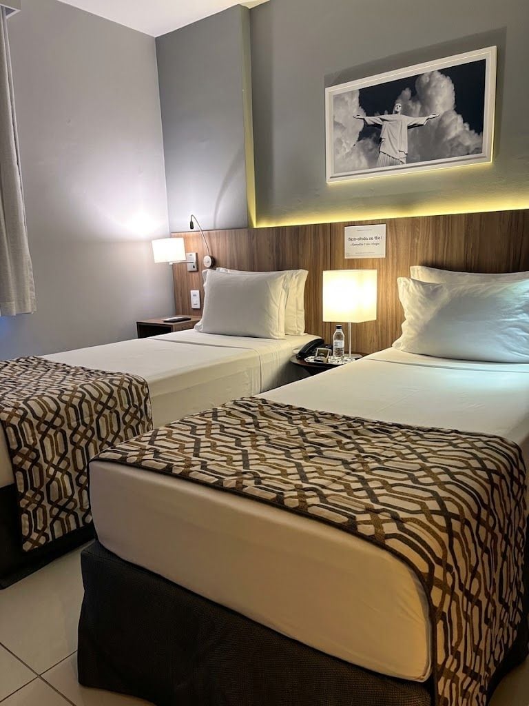 Habitación de hotel con dos camas, una mesita de noche, una lámpara y un cuadro en la pared.