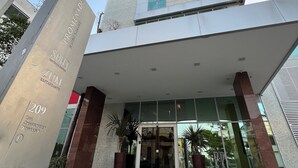 A modern building with a prominent entrance, large glass windows, and a stone pillar with text. - Promenade Soho Campos dos Goytacazes (Campos)