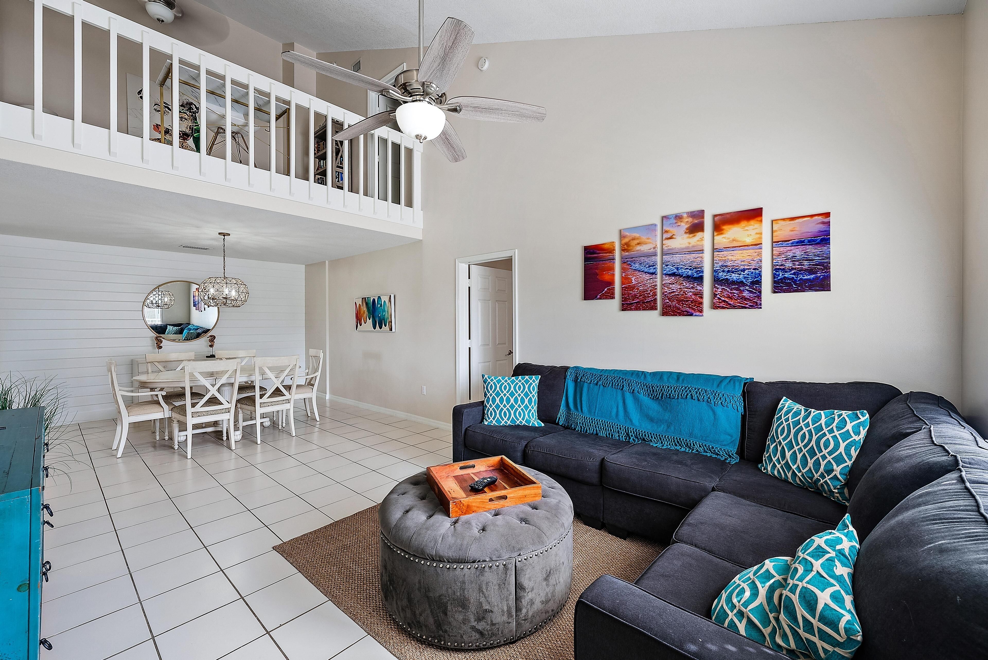 A spacious living room with a dark sofa, ottoman, and a dining area with a white table and chairs.