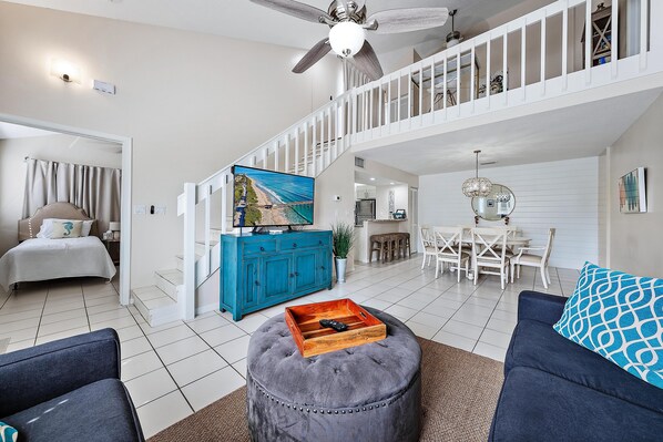 A spacious living room with a high ceiling, a staircase, and a dining area.