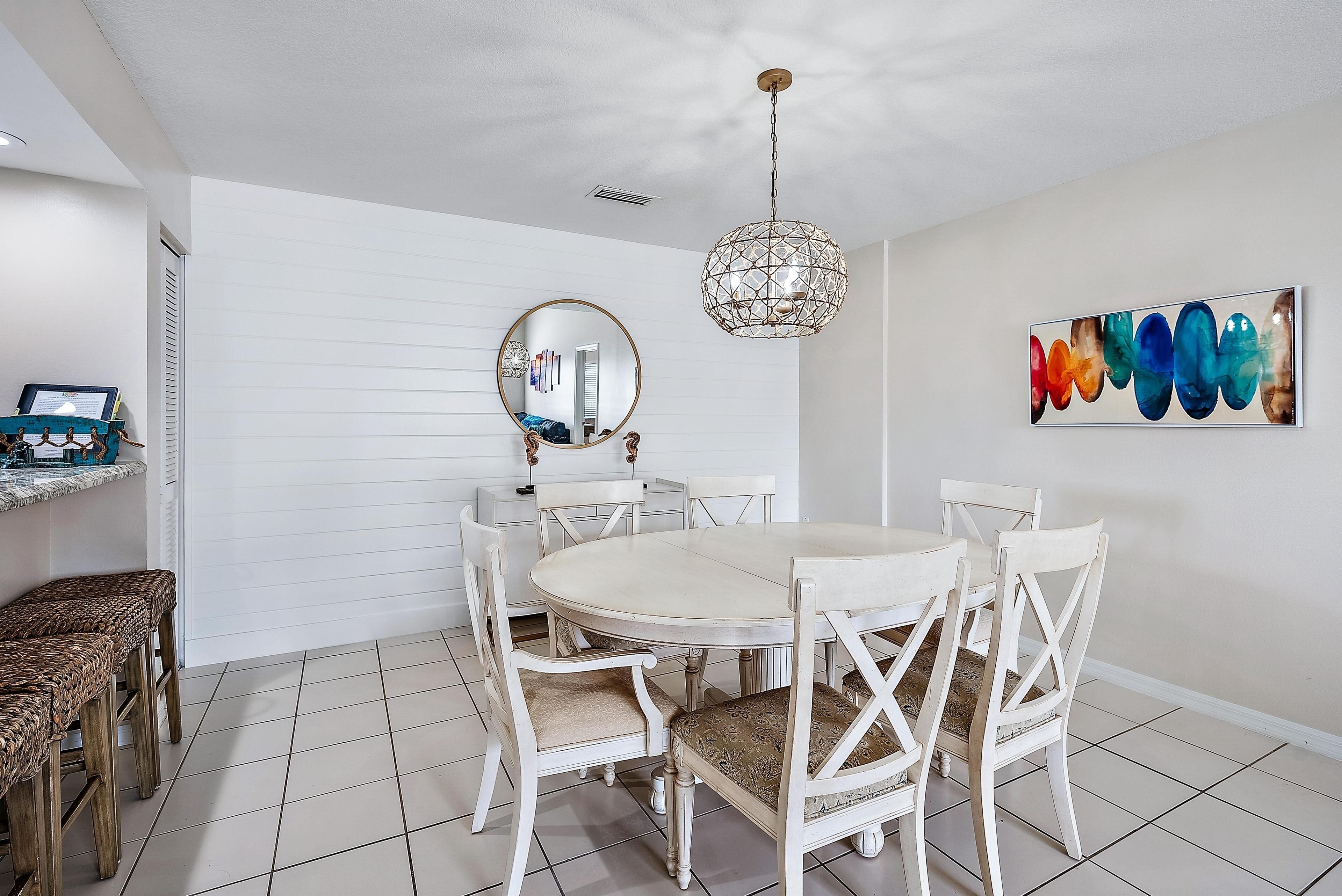 A dining area with a round table, white chairs, and a hanging light fixture.